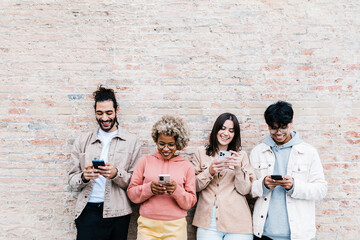 Four multiracial people using mobile phone outdoors - Addicted young friends chatting to cell phone social media app