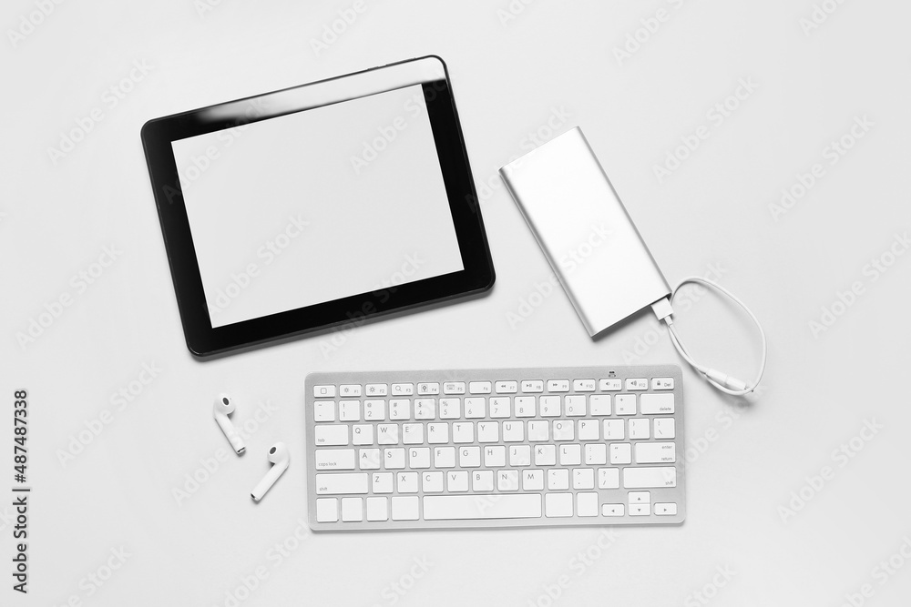 Tablet computer, power bank, earphones and keyboard on white background