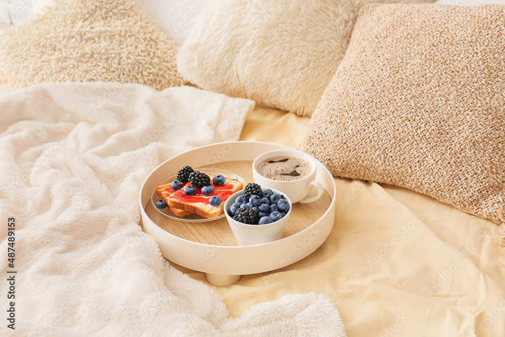 Tray with tasty breakfast on comfortable bed