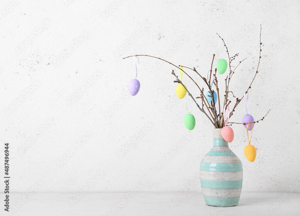 Vase with tree branches and different Easter eggs on light background