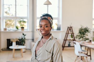 Wall Mural - Portrait of smiling young Afro-American woman in headscarf and round earrings standing in modern coworking space