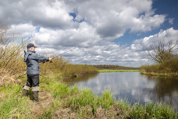 Wall Mural - Fisherman in a jacket throws a spinning rod.