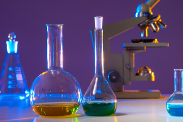 Poster - Glassware laboratory close-up. Biologist's desktop. Flasks with multi-colored liquids. Reagents of laboratory assistant of biologist. Microscope in background. Glassware laboratory on purple.