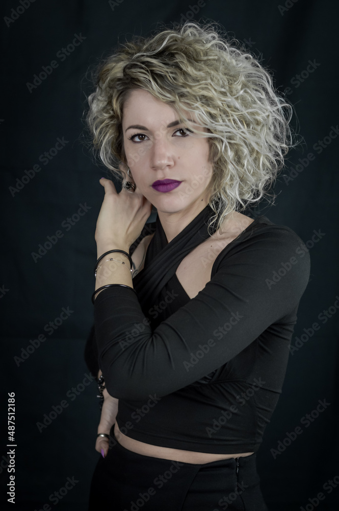 Portrait of a beautiful young curly blonde woman who adjusts her hair ...