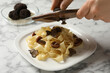 Woman slicing truffle onto tagliatelle at white marble table, closeup