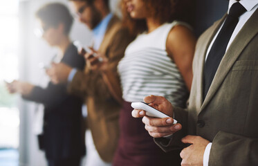 Poster - Keep track of industry developments just by logging in. Shot of a businessperson using his cellphone with colleagues blurred in the background.