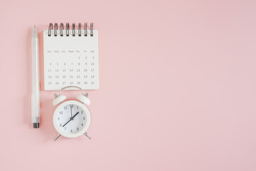 Wall Mural - white opened small calendar, analog alarm clock and pen, top view, with copy space on sweet pink background