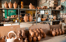 Various Handmade Utensils From Baked Clay On Floor And On Racks In Pottery Workshop