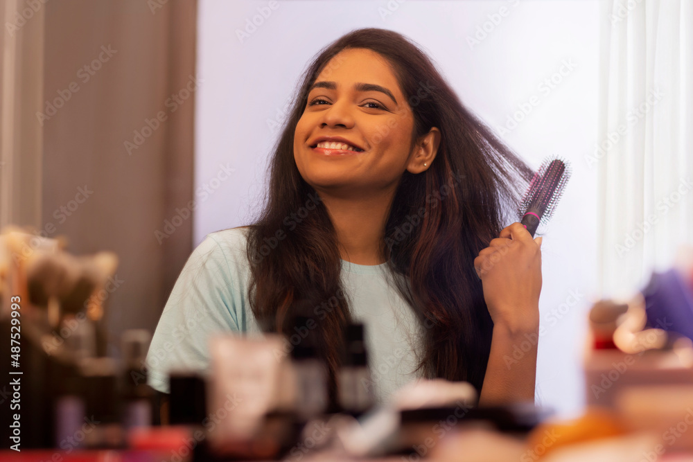Young woman combing her hair in front of mirror Stock Photo | Adobe Stock