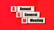 On a bright red background, wooden cubes and blocks with the text AGM Annual General Meeting. Manufacturing of wooden toys.