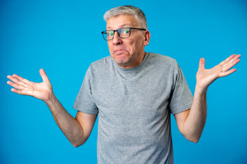 Middle age man over blue background clueless and confused expression with arms raised