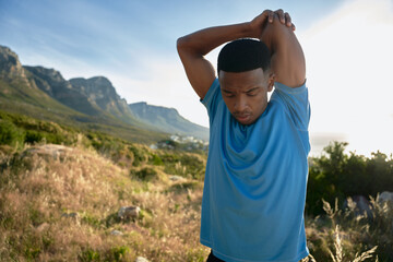 Black young Adult male looking down while stretching before his run on the mountain in the morning