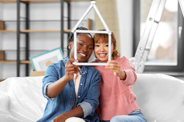 moving, people and real estate concept - happy smiling women with ruler folded in shape of house at new home