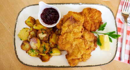 Wall Mural - Saftiger Wiener Schnitzel vom Kalb mit wellen Panade und Bratkartoffeln auf schönem Teller 