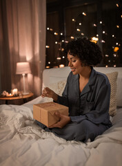 Sticker - holidays, christmas and people concept - happy smiling woman in pajamas with gift box sitting in bed at night