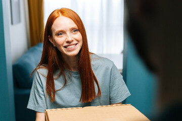 Close-up face of happy young woman receiving paper boxes with hot pizza from delivery man on doorway at home. Back view of courier male delivering boxes with food to female client at apartment.