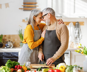 Happy elderly family couple wife and husband embracing while cooking vegetarian food together