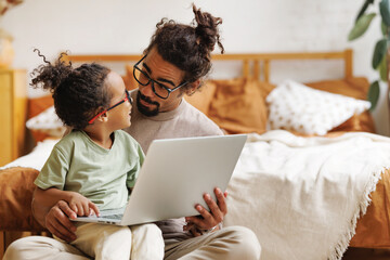 Happy african american family little son with dad watching funny videos on laptop together at home