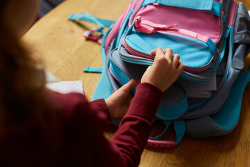 Schoolgirl put books and notes into backpack at home, pupil prepare staff for education