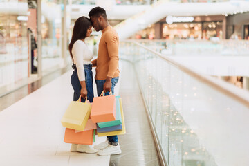 Wall Mural - Cheerful young black couple hugging and holding shopping bags