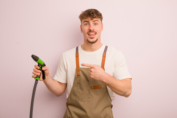 Wall Mural - young cool man looking excited and surprised pointing to the side. gardener and hose concept