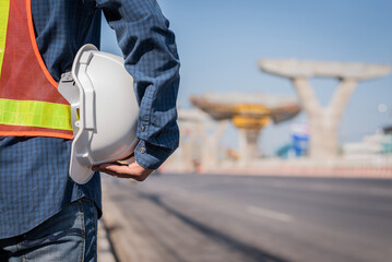  view from behind, white hard hat in hand of male worker on road construction background