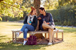© Monkey Business - Smiling Couple Sitting On Bench In Autumn Park With Reusable Drinks Cups