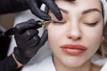 Wall Mural - Close-up of a woman, in a beauty salon with her eyes closed, a cosmetologist makes permanent eyeliner makeup. Professional in black gloves and with a special too