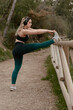 © MiguelZare - Young fitness woman listens to music with headphones and does stretching exercises outdoors