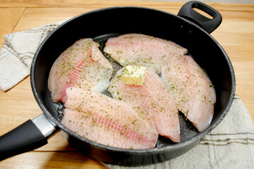 Wall Mural - Fresh Tilapia Frying in a Black Pan with Butter and Herbs