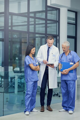 Canvas Print - Comparing diagnosis. Shot of a group of doctors talking together over a digital tablet while standing in a hospital.