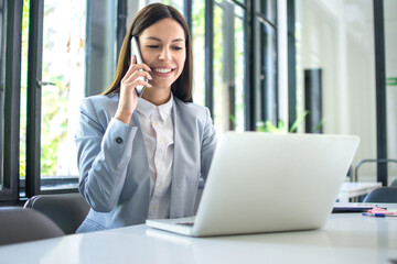 Beautiful businesswoman talking on mobile phone and using laptop in office