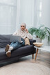 © LIGHTFIELD STUDIOS - cheerful arabian woman in hijab eating popcorn and watching film on laptop on couch.