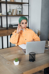 Wall Mural - muslim woman raising hand during online lesson at home.