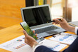 © ArLawKa - Businessman holding a mobile smartphone work on a laptop computer Analyzing, calculating, graphing, business data in the office, reviewing profit reports. business strategy ideas