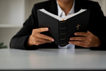 Close-up of black leather with a Christian cross in the hand of a woman in black holding a Bible in her heart with her heart. Religious concepts and holidays