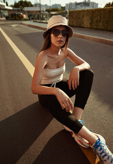 Wall Mural - Trendy young lady sitting on asphalt road in sunlight