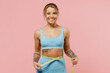 © ViDi Studio - Young fun strong sporty athletic fitness trainer instructor woman wear blue tracksuit spend time in home gym hold measure tape on waist isolated on pastel plain pink background. Workout sport concept.