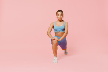 Full length young sporty athletic fitness trainer woman wear blue tracksuit spend time in home gym train do stretch legs squat exercise isolated on plain light pink background. Workout sport concept.