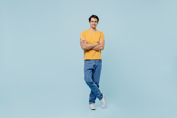 Full body smiling happy fun caucasian young man 20s wear yellow t-shirt hold hnads crossed folded look camera isolated on plain pastel light blue background studio portrait. People lifestyle concept.