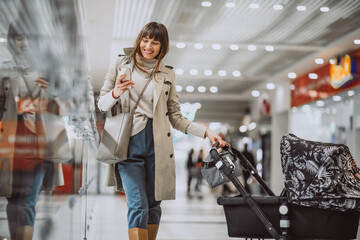 Young mother walking baby stroller in a shopping mall and talking on the phone