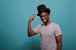 Illusionist pointing at vintage top hat on head for entertainment, doing fun performance with magic and classic costume prop in front of camera. Confident guy with retro topper.