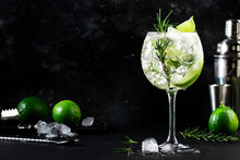 Gin Tonic Alcoholic Cocktail Drink With Dry Gin, Rosemary, Tonic, Lime And Ice Cubes In Wine Glass. Black Bar Counter Background, Bar Tools, Copy Space