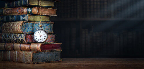 Old clock hanging on a chain on the background of old books.  Сlock as a symbol of time a books are a symbol of knowledge.. Concept on the theme of history, nostalgia, culture.