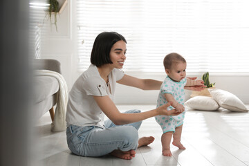 Wall Mural - Mother supporting her baby daughter while she learning to walk at home