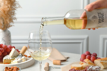 Canvas Print - Woman pouring white wine from bottle into glass at table with snacks, closeup