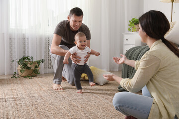 Wall Mural - Parents supporting their baby daughter while she learning to walk at home