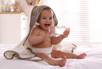 Canvas Print - Cute little baby with towel and bottle of massage oil on bed at home