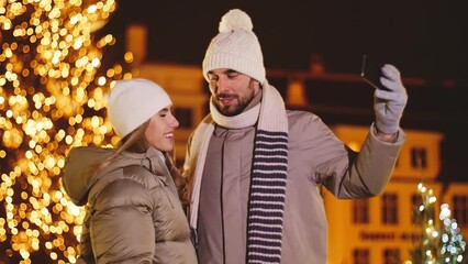 Sticker - winter holidays, leisure and people concept - happy couple taking selfie with smartphone in city over christmas lights