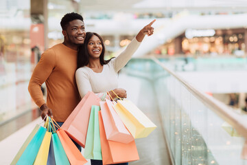 Wall Mural - Portrait of black couple with shopping bags pointing at window